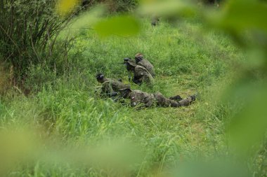 Bir grup maskeli insan ormanda paintball oynuyor.