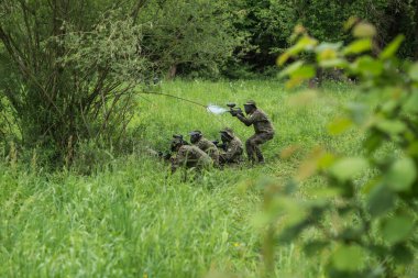 Bir grup maskeli insan ormanda paintball oynuyor.