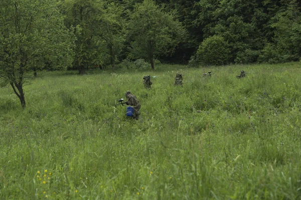 Bir grup maskeli insan ormanda paintball oynuyor.