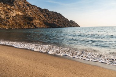 Waves crashing on the sandy beach in the bay between the hills
