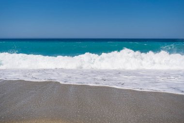 Mavi Akdeniz 'in dalgalarının kumlu bir sahile çarptığı bir manzara.