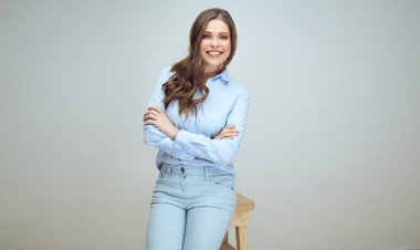 Gülümseyen genç bir kadın kollarını kavuşturarak tabureye oturur. izole edilmiş stüdyo resmi.