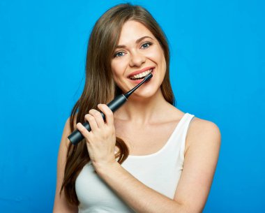 Gülümseyen kadın elektrikli diş fırçasıyla diş temizliyor. Mavi üzerine izole edilmiş bir portre..