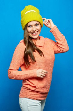 Sarı şapkalı pembe kapüşonlu genç bir kadın. Mavi arka planda zımparalanan sıradan giyinmiş bir kızın portresi.