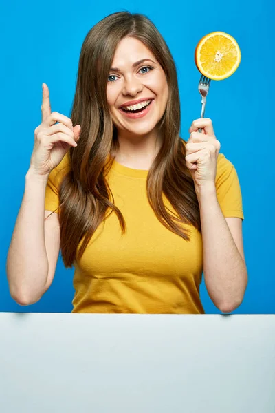 オレンジ色の果実と指差し指でフォークを保持笑顔女性 青い背景にコピースペースのあるホワイトボード — ストック写真