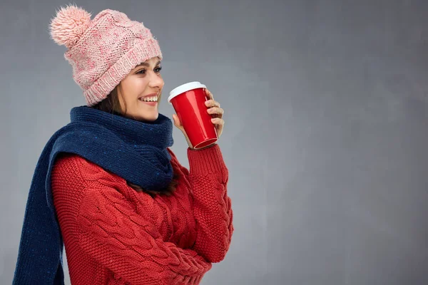 暖かい冬服を着て 赤いコーヒーグラスを持ったニット帽をかぶった女性 灰色のスタジオの肖像画に分離 — ストック写真