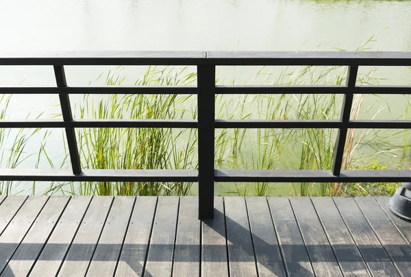 低头看着栏杆的阳台或面临与池塘的木板路 图库照片