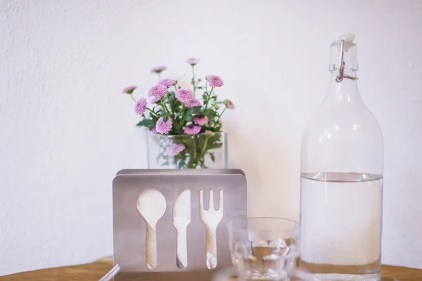 Verfrissend water kruik en bloemen op tafel tegen witte muur. — Stockfoto