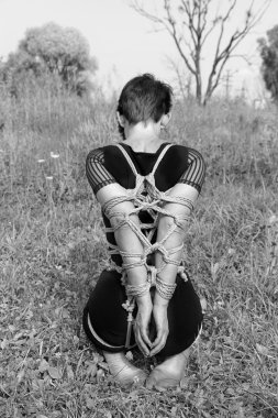Diz çökmüş kadına bağlı. Siyah-beyaz fotoğraf, Shibari.