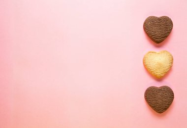 Pembe arka planda üç pişmiş kalp şeklinde kurabiye..