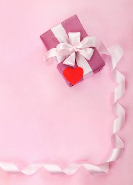 Pembe hediye kutusu, beyaz fiyonk, uzun kıvrımlı kurdele, kağıt kırmızı kalp ve metin için boş alan.