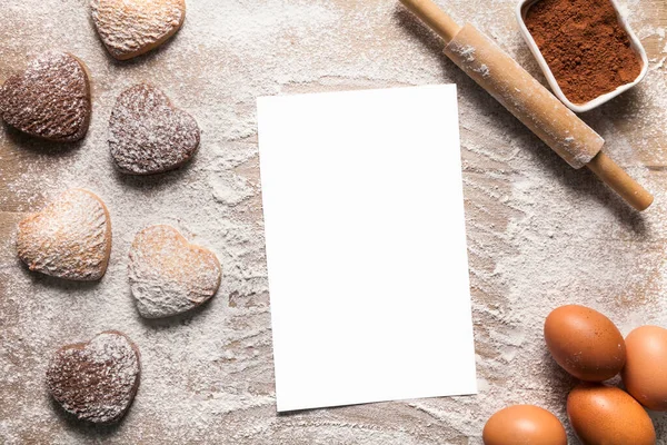 Fundo de cozimento com folha de papel em branco para a receita ou menu, biscoitos em forma de coração, ovos, farinha e rolo. Imagens De Bancos De Imagens Sem Royalties