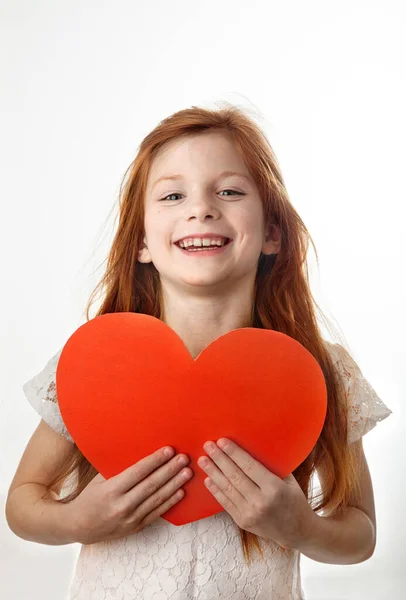 Ritratto di bambina dai capelli rossi con un grande cuore rosso tra le mani. Foto Stock Royalty Free