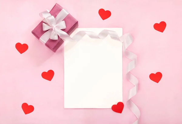 Valentines day greeting card with pink gift box, white bow, long curved ribbon and paper red hearts. — Stok Foto