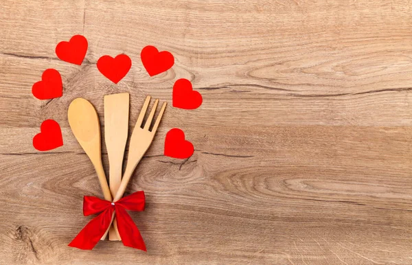 赤い弓を持つ木製の台所用品 木の背景に紙の赤い心とテキストのための空のスペース スプーン へらを調理し フォーク バレンタインデーキッチンの背景 愛と料理 トップビュー フラットレイアウト — ストック写真