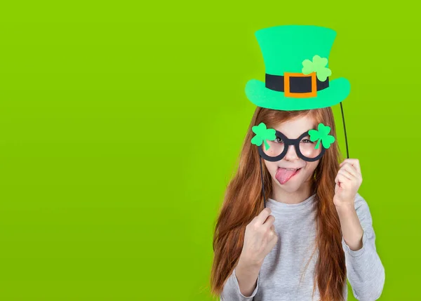 Poco sonriente caucásico pelirroja chica en verde sombrero de duende y trébol de trébol vasos sobresaliendo lengua —  Fotos de Stock