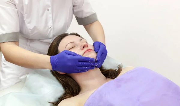 美容院实施按摩疗法的高加索女性患者的美容手戴蓝色手套触摸脸. — 图库照片