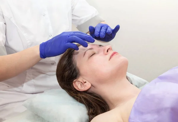 Le mani di cosmetologo in guanti azzurri toccano la faccia di paziente di donna caucasica che fa la procedura di massaggio in salone di bellezza. — Foto Stock