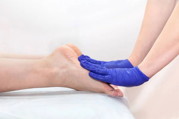 Massaggiatore mani in blu guanti protettivi toccare i piedi della paziente donna facendo procedura di massaggio ai piedi nel salone spa. — Foto Stock