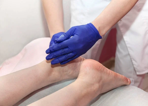 Massaggiatore mani in blu guanti protettivi toccare i piedi della paziente donna facendo procedura di massaggio ai piedi nel salone spa. — Foto Stock