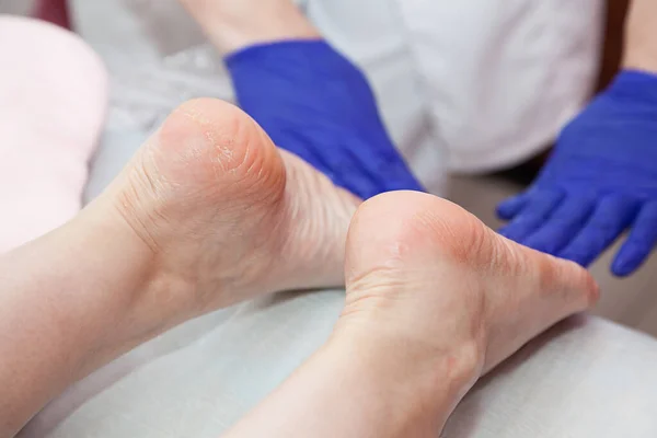 Massaggiatore mani in blu guanti protettivi toccare i piedi della paziente donna facendo procedura di massaggio ai piedi nel salone spa. — Foto Stock
