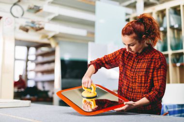 Glazier woman worker holding a glass pane with suction cups in workshop. Industry and manufactory production clipart