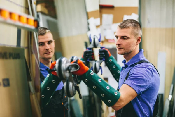 Glazier worker holding a big mirror glass pane in workshop. Industry and manufactory production