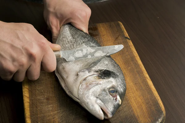 Reiniging van de vis op een houten bord — Stockfoto