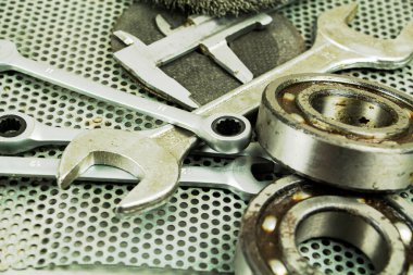 Metal işleme araçları, çelik parçalar, bir ingiliz anahtarı, metal bir kafesin arka planında.