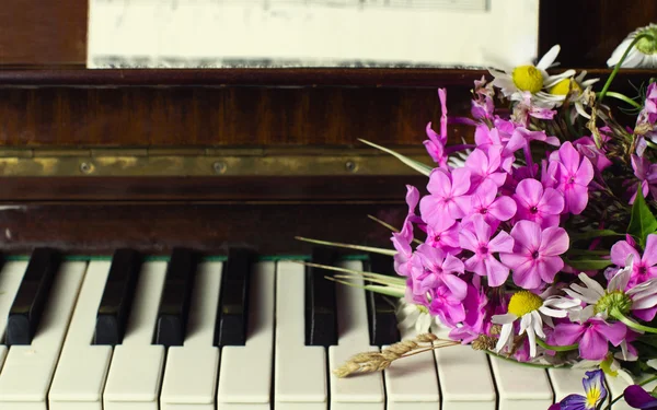 Bukett med sommarblommor på ett piano — Stockfoto