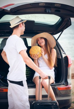 Deniz kıyısındaki açık arabanın yanında duran genç çift.