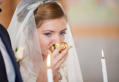 Rahip, Ortodoks düğün töreninde taç giymiş bir geline şarap veriyor.