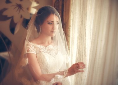 Pencerenin yanında duran beyaz gelinlikli güzel gelin.