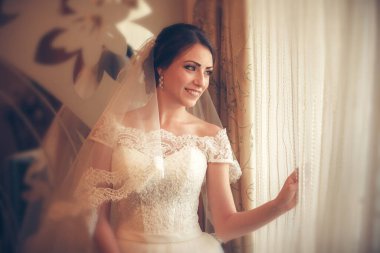 Pencerenin yanında duran beyaz gelinlikli güzel gelin.