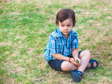 Parktaki çimlerin üzerinde oturan küçük Latin çocuk.