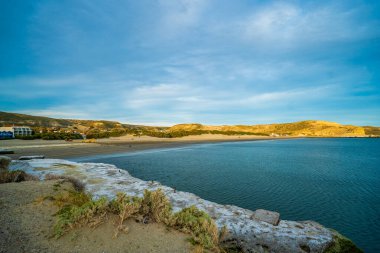 Kayalık bir kıyı şeridi ve bir su kütlesi olan bir sahil. Su mavi ve gökyüzü berrak.
