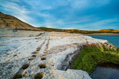 Arka planda mavi gökyüzü olan kayalık bir yamaç. Tepe beyaz kayalarla kaplı.