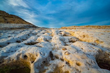 Arka planda mavi gökyüzü olan kayalık bir yamaç. Tepe beyaz kayalarla kaplı.