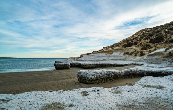 Arka planda su bulunan kayalık bir sahil. Kumsal karla kaplı. Sahilde kayalar var.