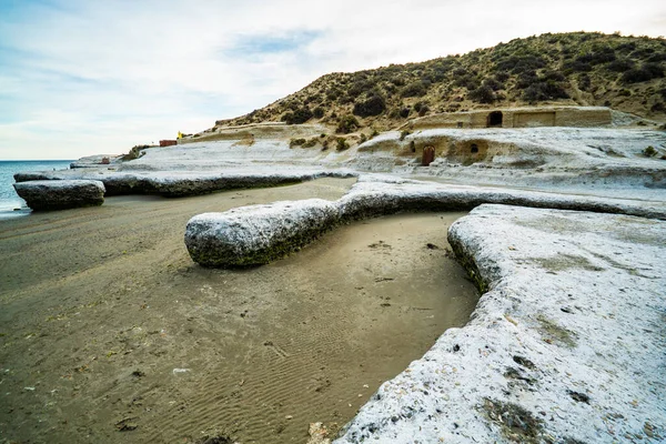 Arka planda su bulunan kayalık bir sahil. Kumsal karla kaplı. Sahilde kayalar var.