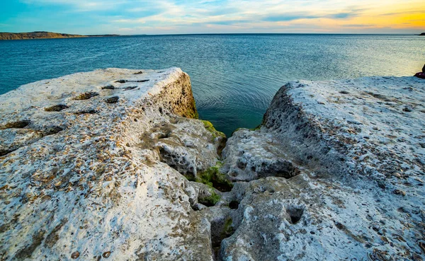Arka planda bir su kütlesi olan kayalık bir kıyı şeridi. Su mavi ve kayalar beyaz.