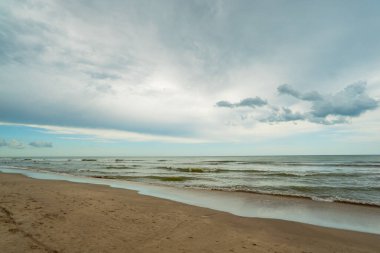 Arka planda bulutlu bir gökyüzü olan bir plaj. Su yeşil ve gökyüzü bulutlu.
