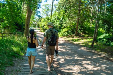 Bir adam ve bir kadın ormanda tahta bir kaldırımda yürüyorlar. Adam sırt çantası takıyor, kadın da siyah gömlek ve şort giyiyor.