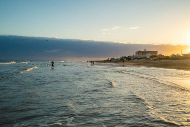 Kumsal güzel ve sakin bir yerdir. İnsanlar okyanusun ve bulutlu gökyüzünün tadını çıkarırlar. Su sakin ve dalgalar yumuşak. Huzurlu bir atmosfer yaratıyor.