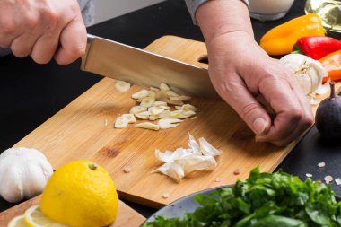 hands of the chef cut the garlic on the cutting board clipart