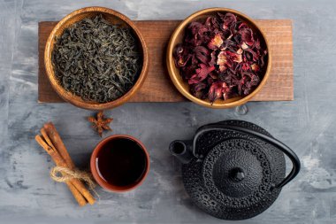 Ahşap fincanlarda kırmızı ve yeşil çay, gri arka planda çaydanlık.