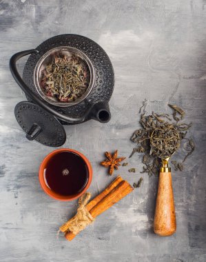 Gri zemin üzerinde yeşil çay bulunan demir çaydanlık.