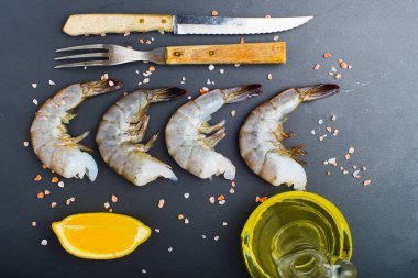 Siyah taşlı arka planda çatal ve bıçaklı çiğ karides. Yukarıdan görünüm