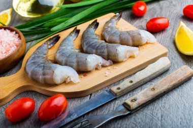 Kesme tahtasında çiğ karides. Bıçak Çatalı. Limon ve yağ.