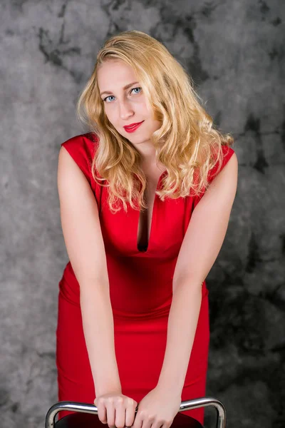 Jovem Loira Vestido Vermelho Segurando Uma Cadeira Fundo Cinza — Fotografia de Stock